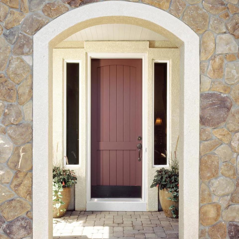 Brick red front door with bronze hardware and kickplate on house with masonry siding.