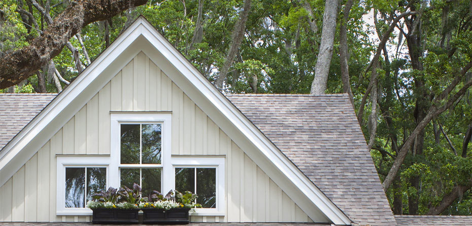 Gable on house with board and batten siding, three small windows with grids, and a flower box