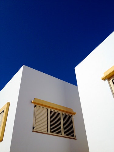 Image of exterior window coverings for additional energy savings. This image shows yellow window shutters on a white building with a dark blue sky.