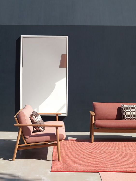 Photo of coral outdoor furniture against a dark background. Furniture includes two outdoor couches, and two overlapping outdoor rugs on a concrete floor.