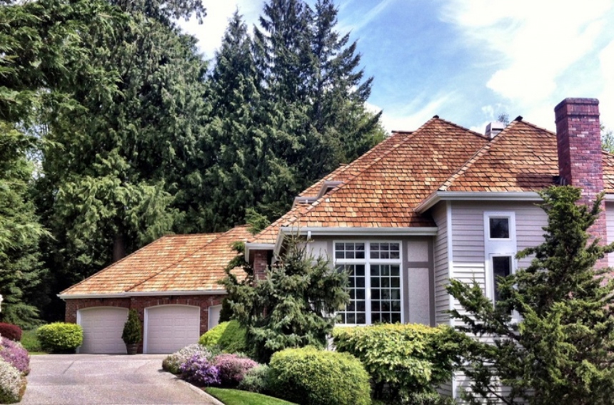 Driveway view of a mixed facade neo-eclectic home with a bright cedar wood shake roof and red brick chimney.