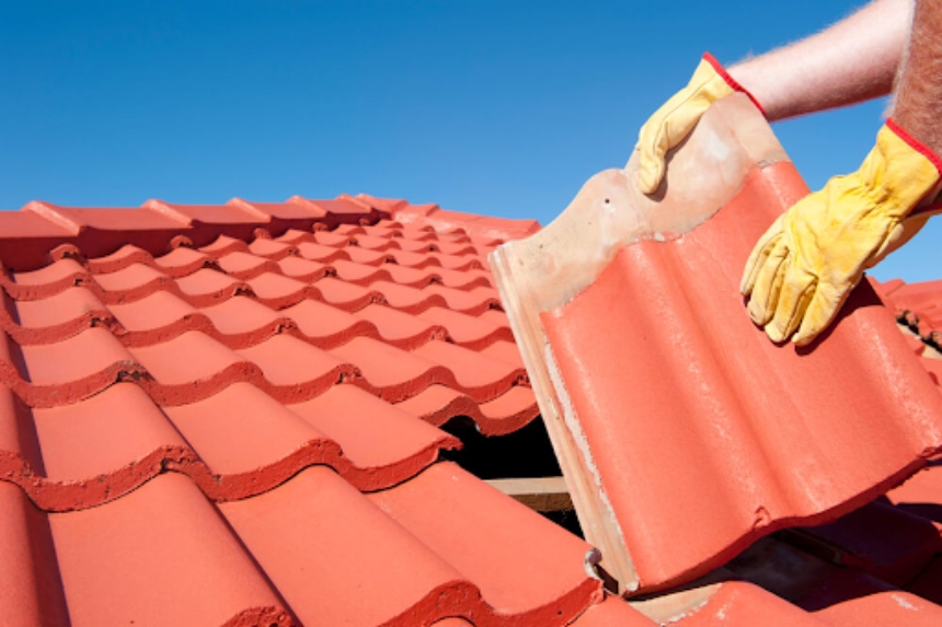 Contractor installing a large red clay tile on a roof covered in s-shape tiles.