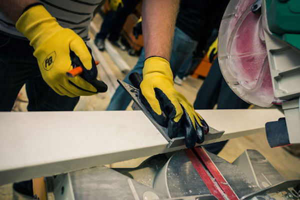 Contractor in yellow gloves measuring a plank